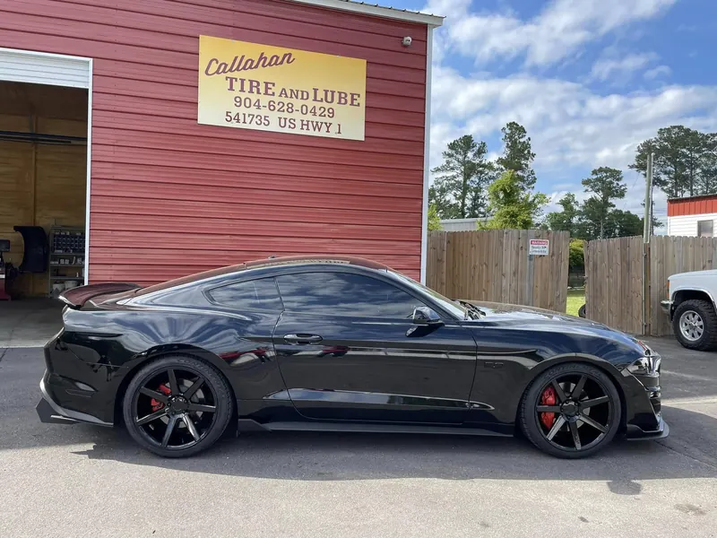 Black Ford Mustang on black wheels with red brake calipers under the Callahan Tire and Lube sign