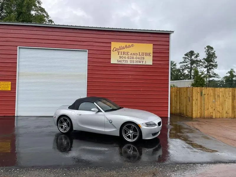Silver BMW Z4 roadster on wet pavement in front of a roll-up door and the Callahan Tire and Lube sign