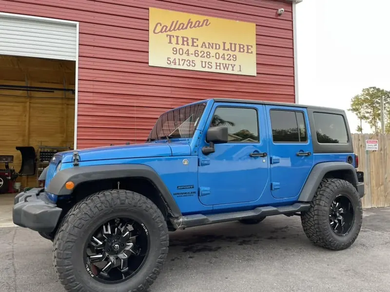 Blue Jeep Wrangler Unlimited on Fuel wheels and mud tires in front of an open bay and the Callahan Tire and Lube sign