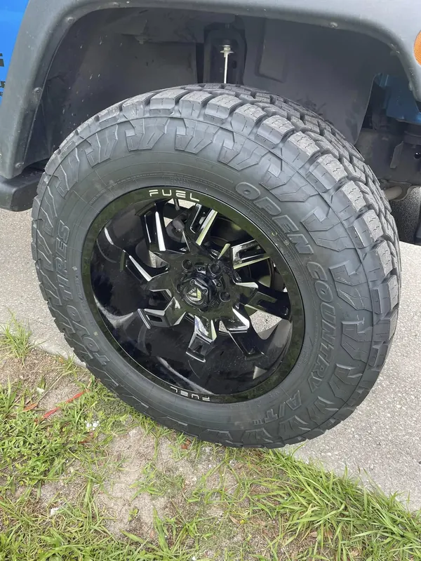 Close-up of a black Fuel wheel and a Toyo Open Country tire on a blue Jeep
