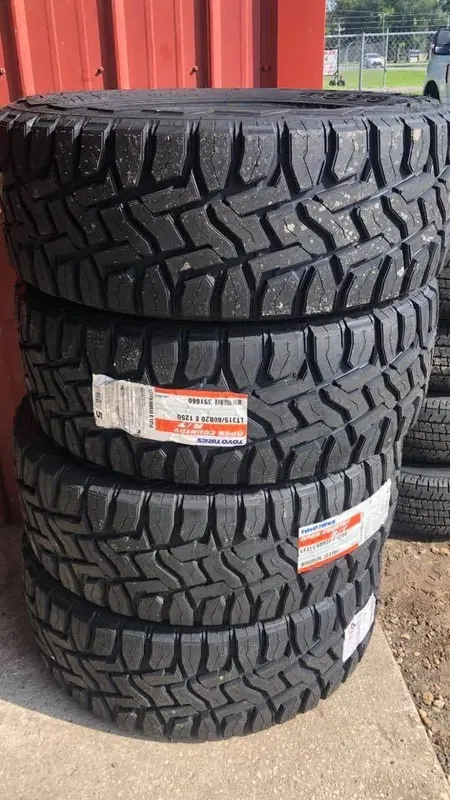 Four new Toyo Open Country R/T tires stacked against the red shop wall