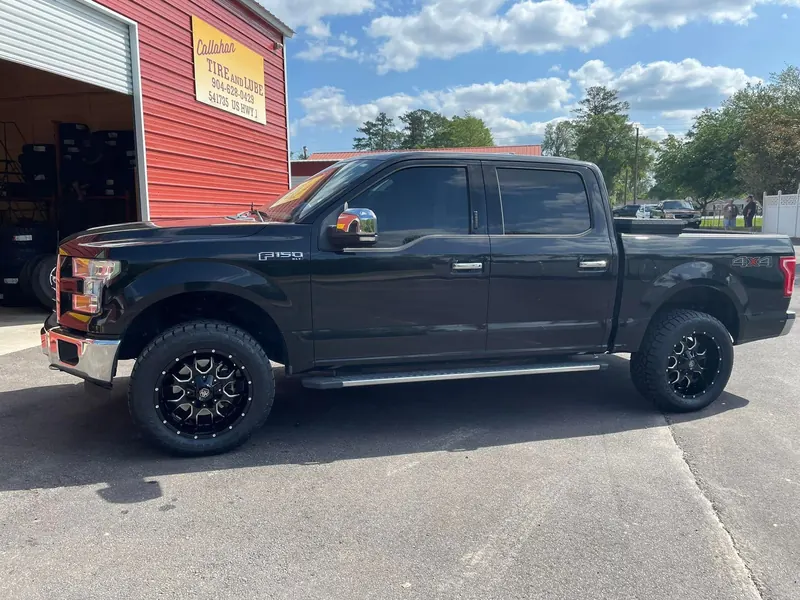Black Ford F-150 XLT on black wheels beside an open bay and the Callahan Tire and Lube sign