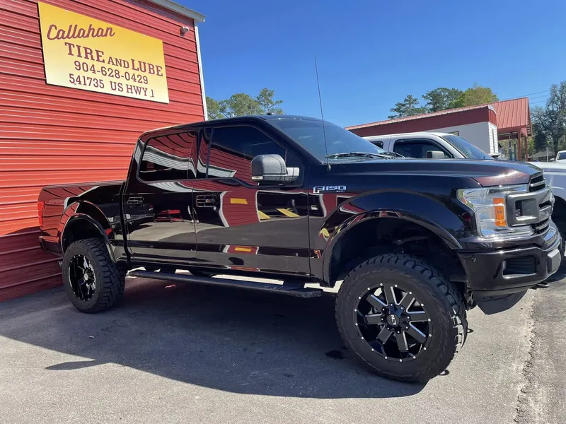 Lifted black Ford F-150 XLT on big mud tires, parked against the red wall under the Callahan Tire and Lube sign