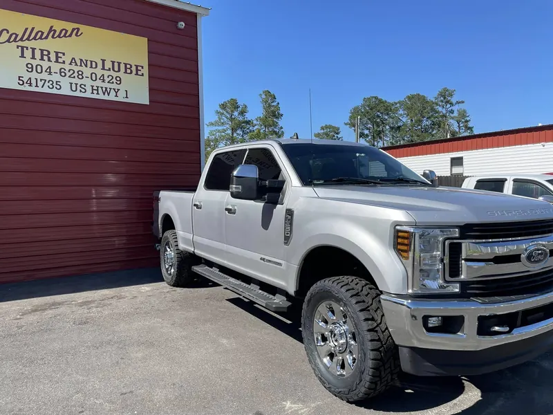 Silver Ford F-250 Super Duty on chrome wheels and mud-terrain tires under the Callahan Tire and Lube sign