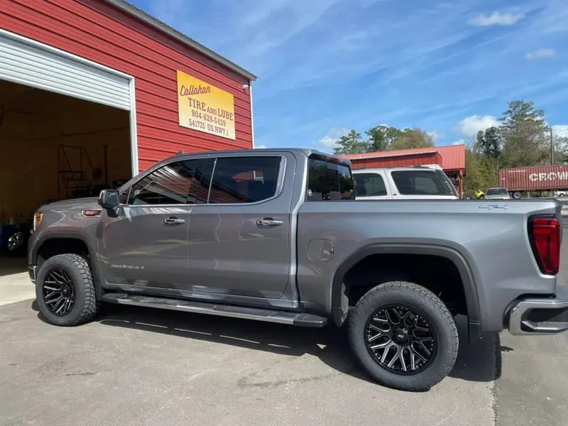 Gray GMC Sierra on black wheels beside an open bay, the Callahan Tire and Lube sign above