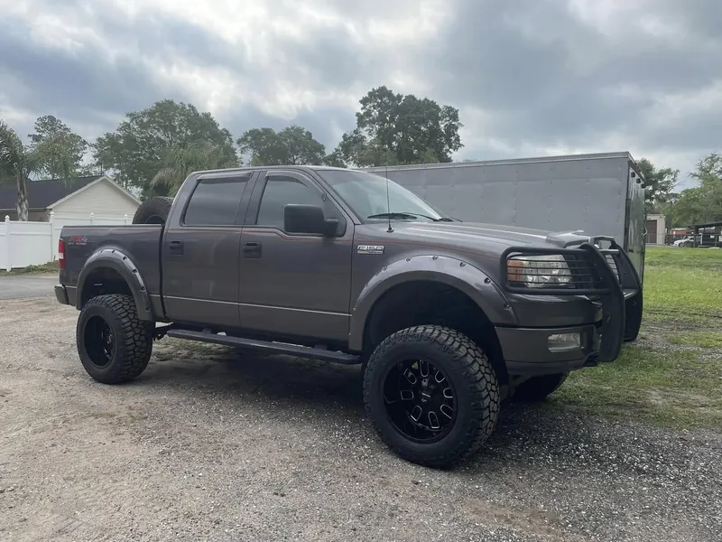 Lifted dark-gray Ford F-150 FX4 with a grille guard, black wheels and mud tires